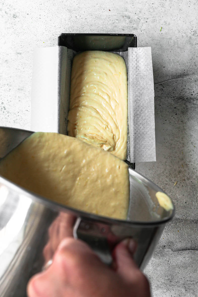 Overhead shot of a hand filling the cake tin with the lemon cake batter