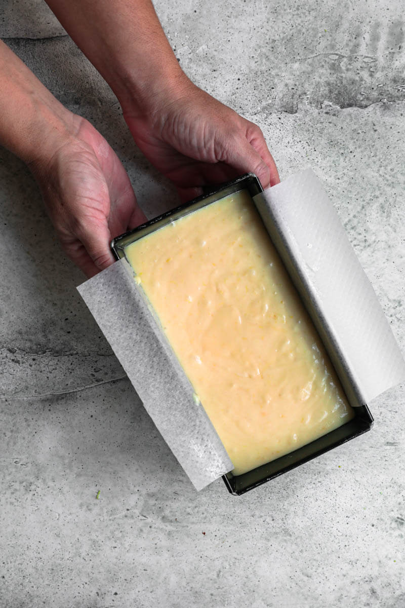 Overhead shot of 2 hands holding the cake tin filled with the batter ready for the oven