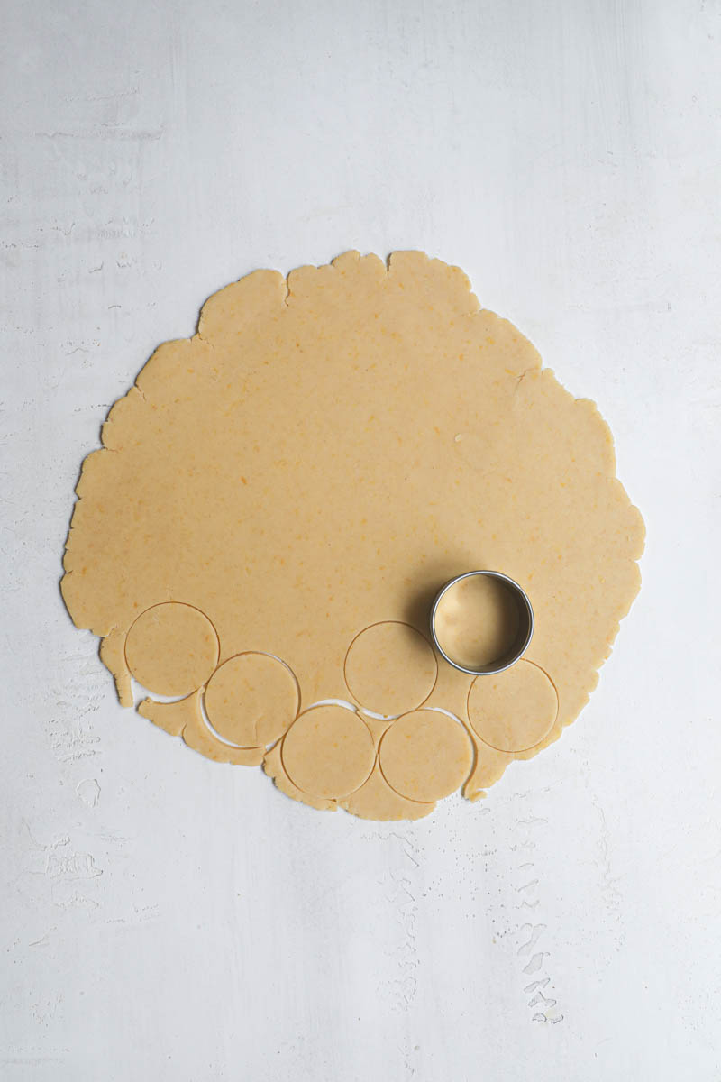 The rolled-out lemon cookie dough with a cookie cutter on top and some cookies cut out from the dough.