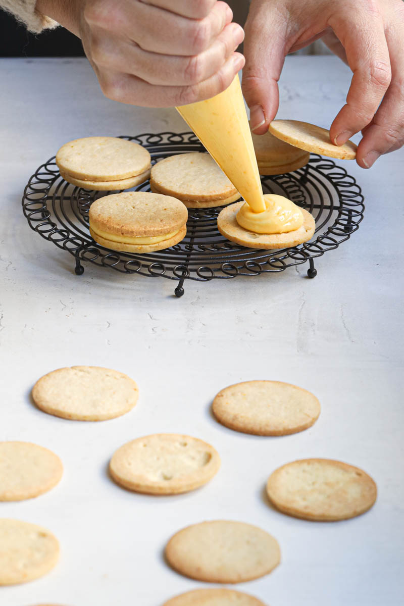 One hand piping lemon curd onto the lemon curd filled cookies.