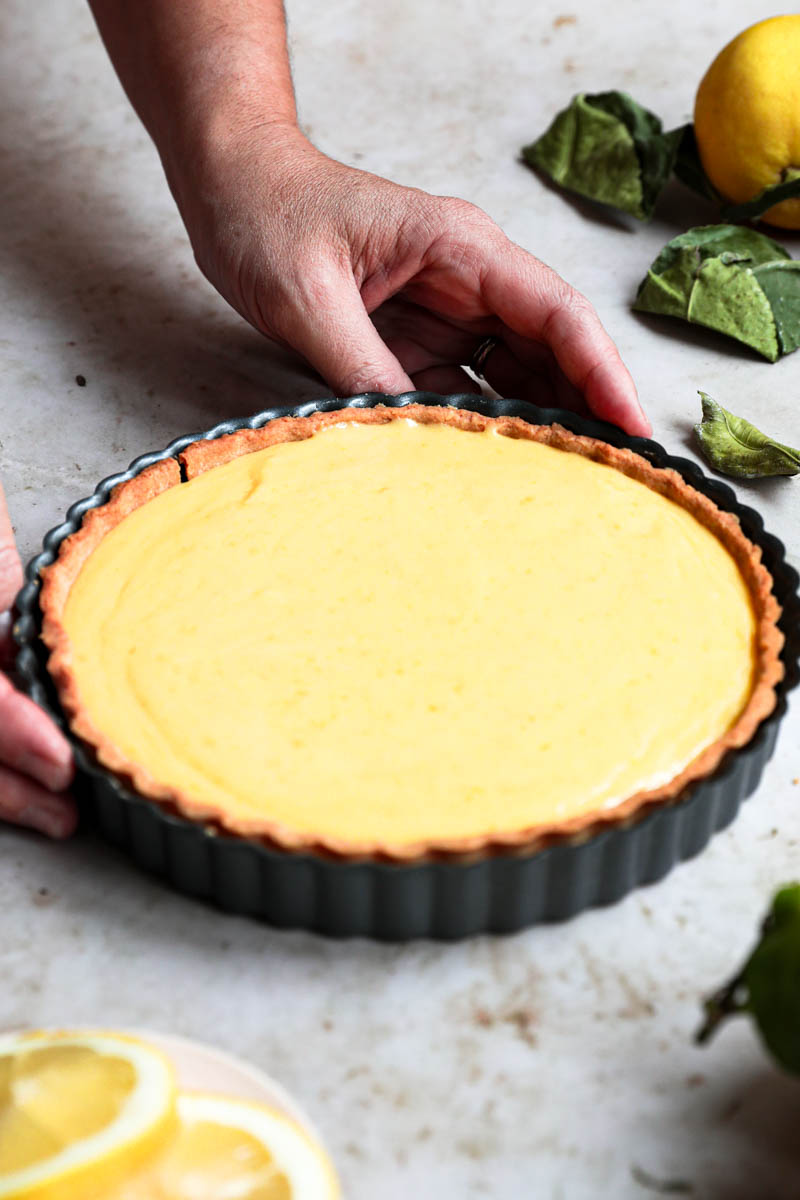 Two hands holding the lemon curd tart before placing in the refrigerator to chill.