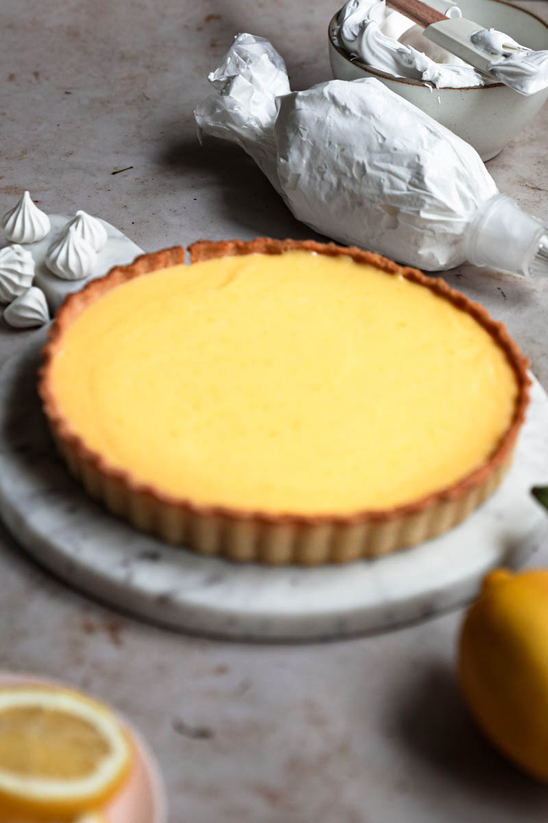 Closeup of the lemon curd tart after chilling with lemons, meringues and pipping bag surrounding it.