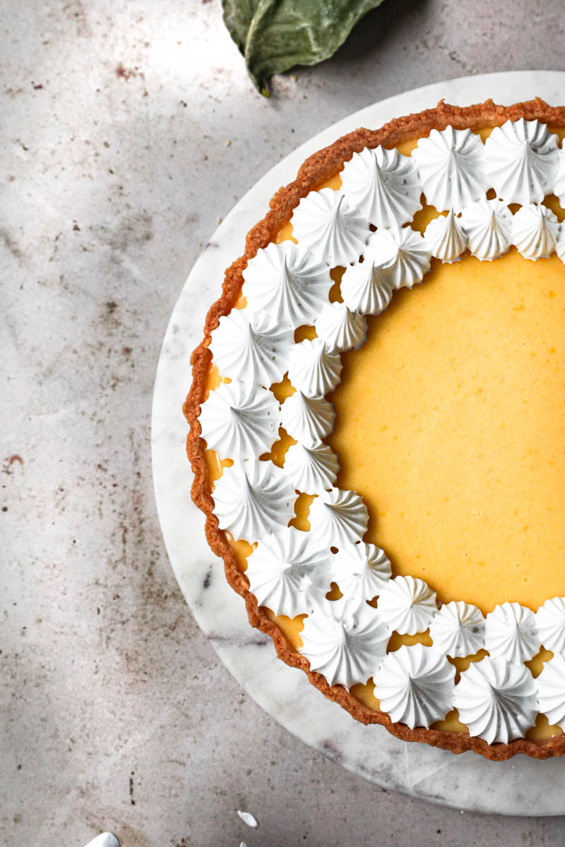 Closeup of half the lemon curd tart with meringue on a marble platter seen from above.