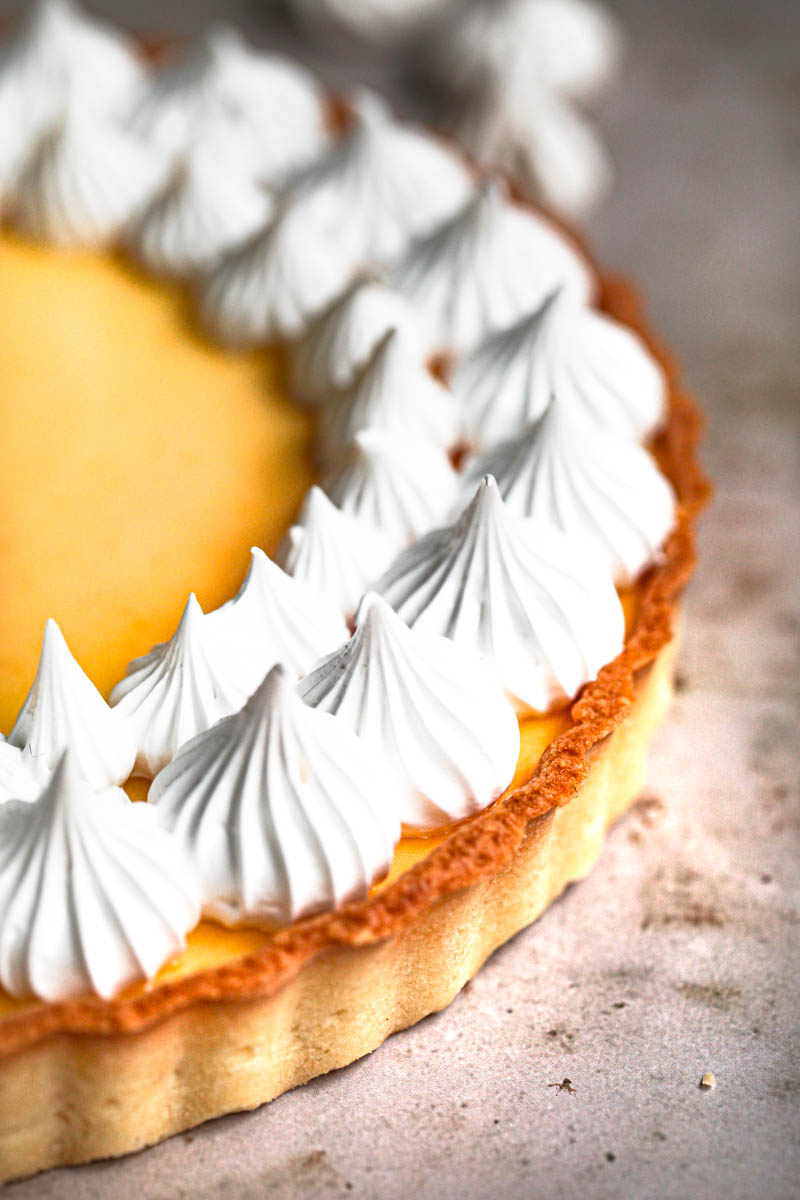 Closeup of half the lemon curd tart on a marble platter seen from the side.