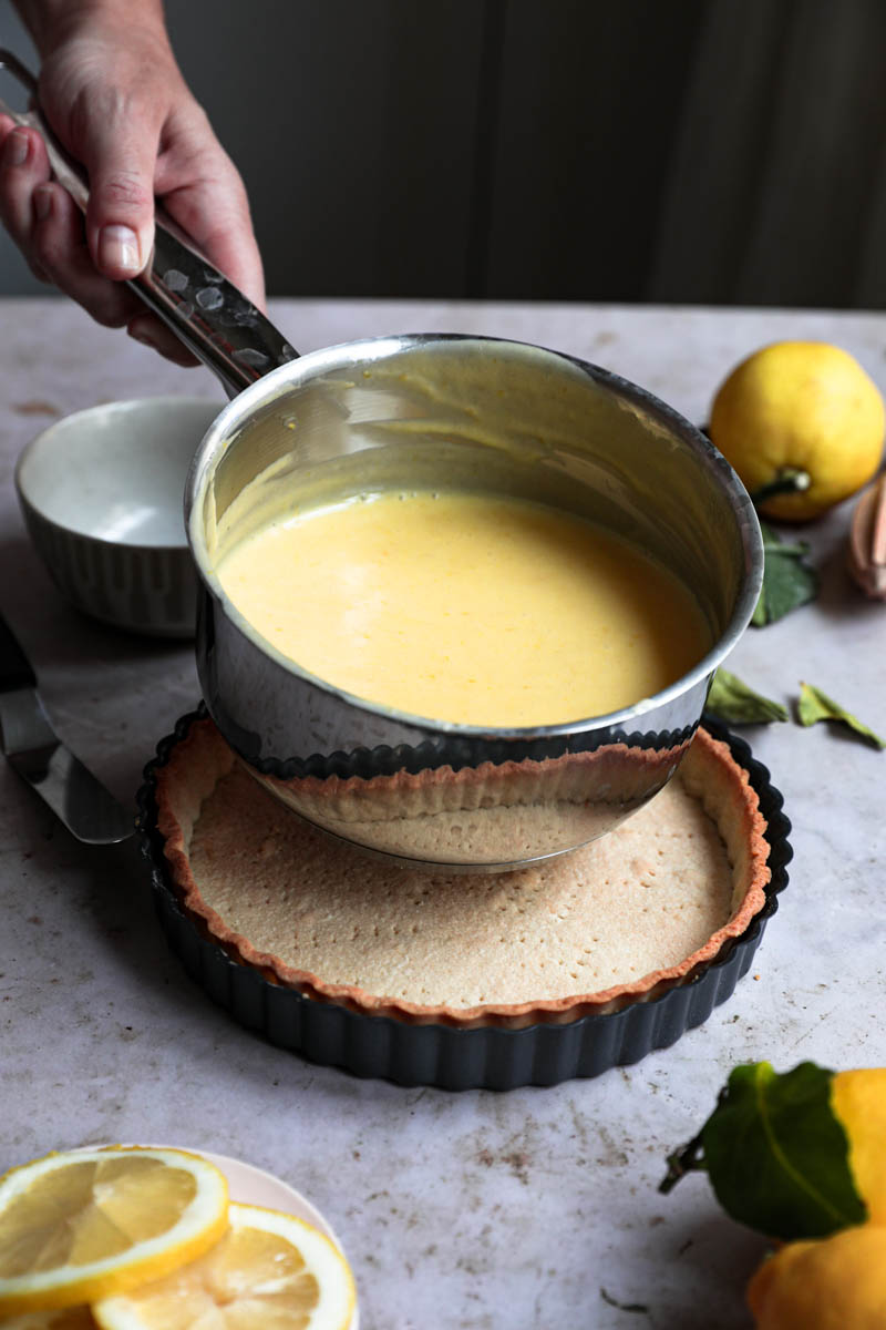 Two hands holding the lemon curd ready inside a large pan.