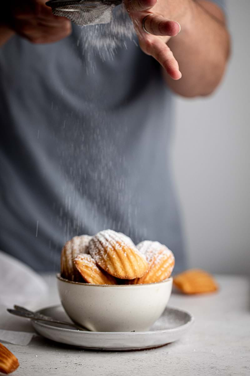 Dusting powdered sugar over madeleines