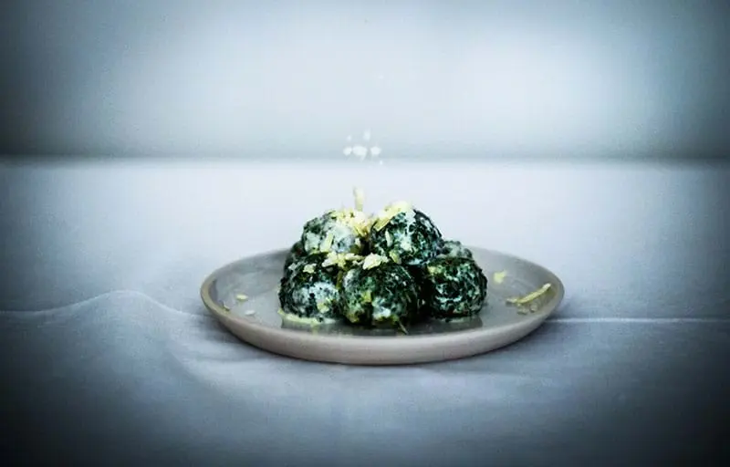 90° shot of the spinach malfatti on a plate with cream and parmesan cheese