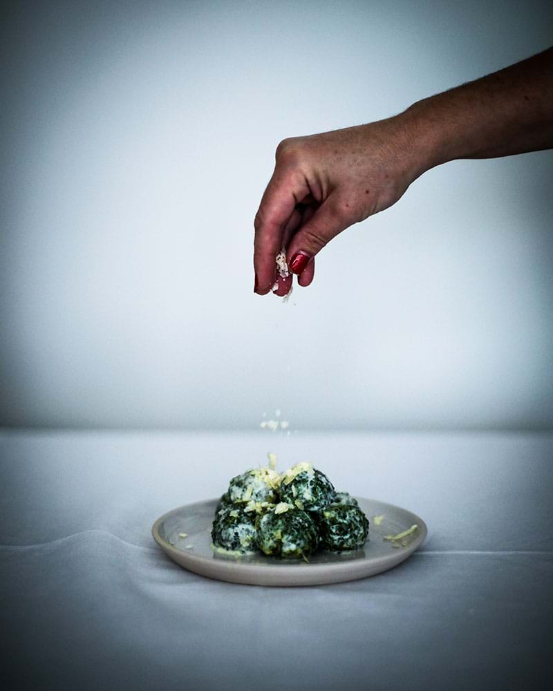 A hand sprinkling the malfatti with parmesan cheese