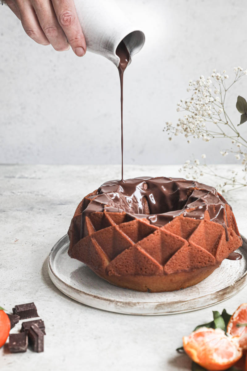 1 hand pouring chocolate ganache over the mandarin orange Bundt cake.