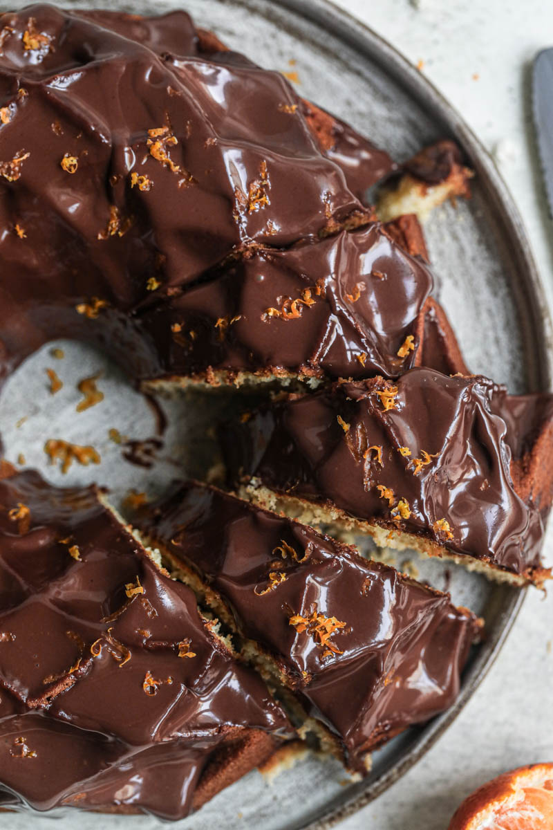 1 hand pouring chocolate ganache over the mandarin orange Bundt cake.