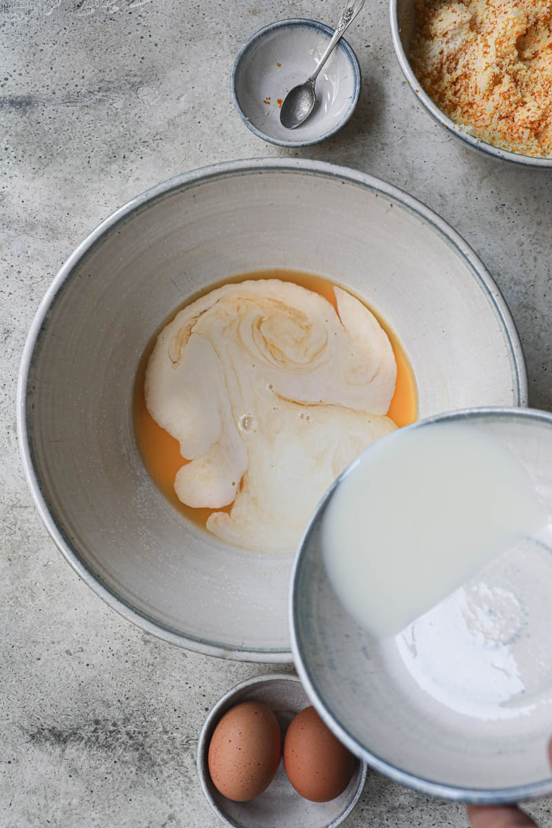 One hand pouring the milk into the bowl with the orange juice and mandarin juice.