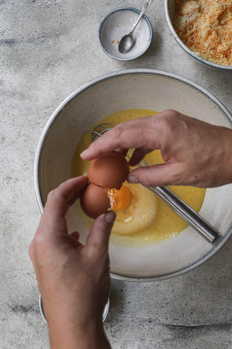 2 hands breaking an egg into the mandarin cake batter.