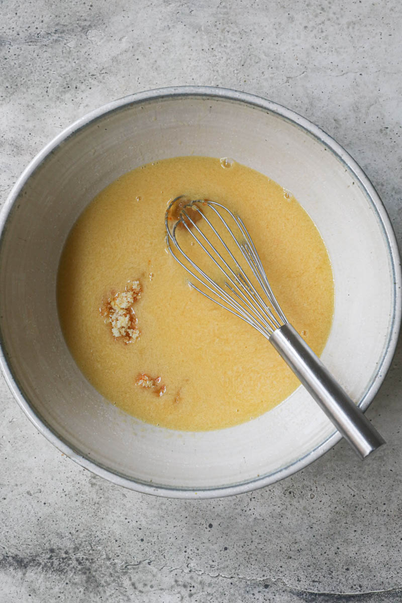 The sugar, the zest, and the liquid ingredient inside a grey bowl with a whisk inside.