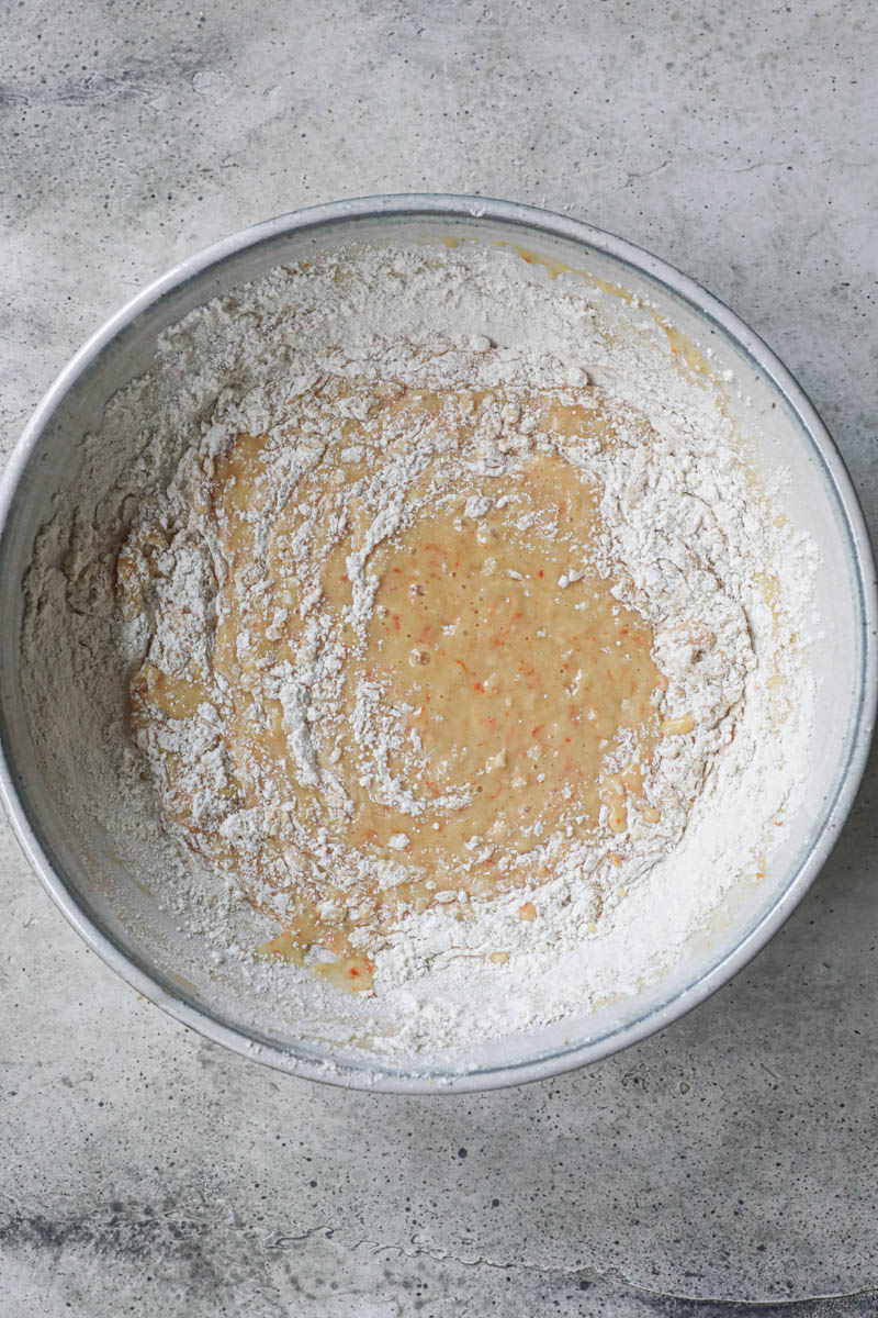 The flour added into the mandarin cake batter inside a grey ceramic bowl.