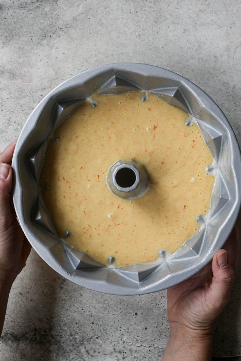 Two hands holding a Bundt cake pan filled with the mandarin orange cake batter.