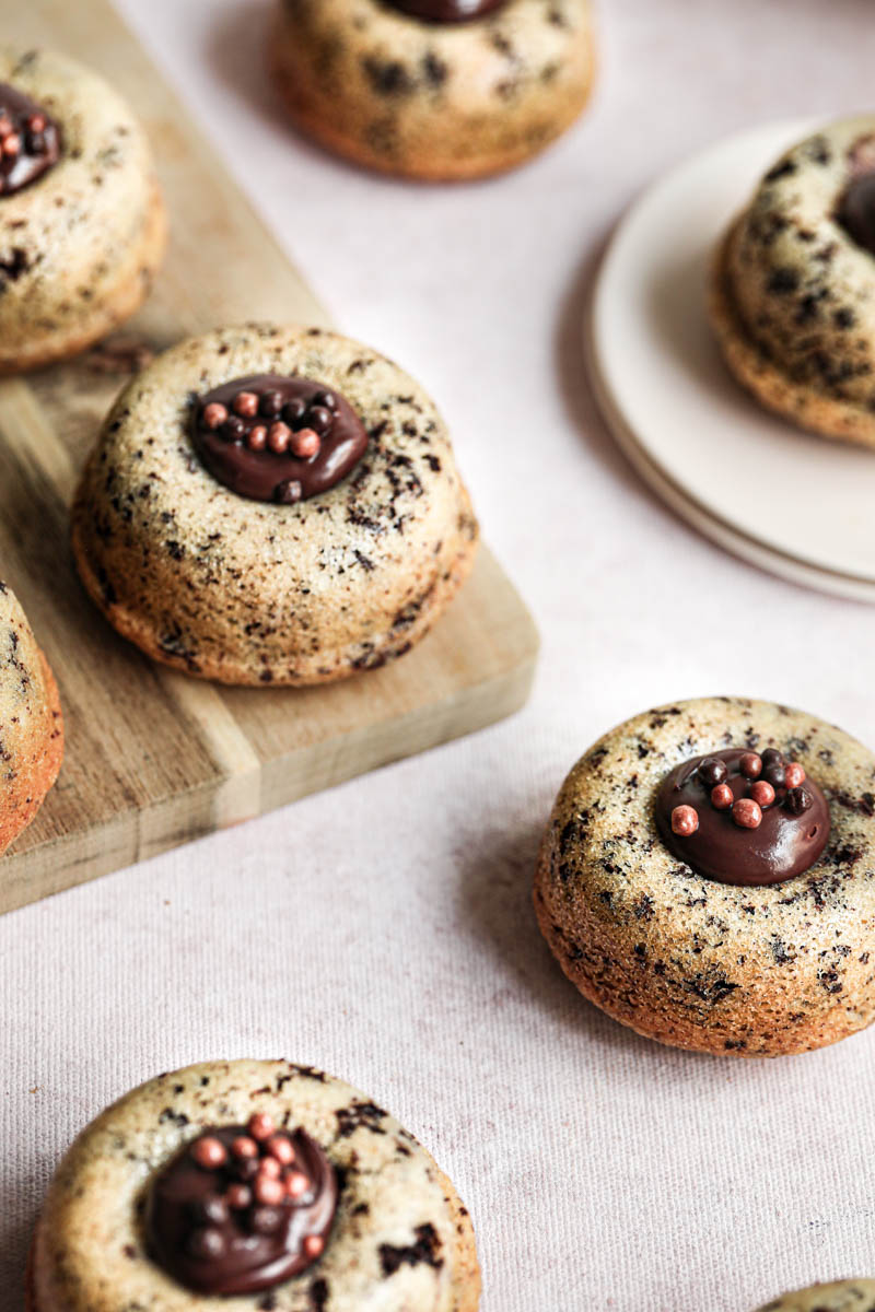 The mini chocolate chip financier almond cakes filled with chocolate ganache arranged on a pink surface, and a wooden chopping board.