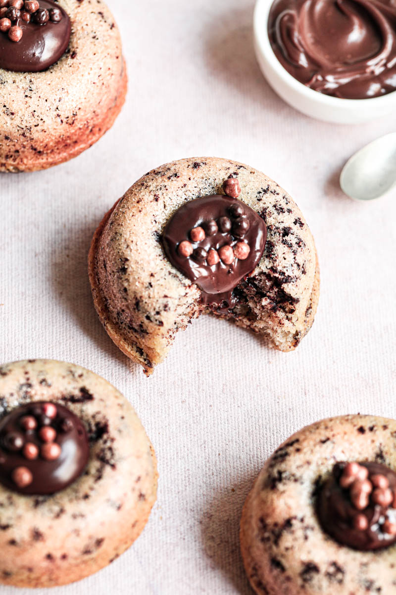 One eaten mini chocolate chip financier almond cake filled with chocolate ganache on others surrounding it.