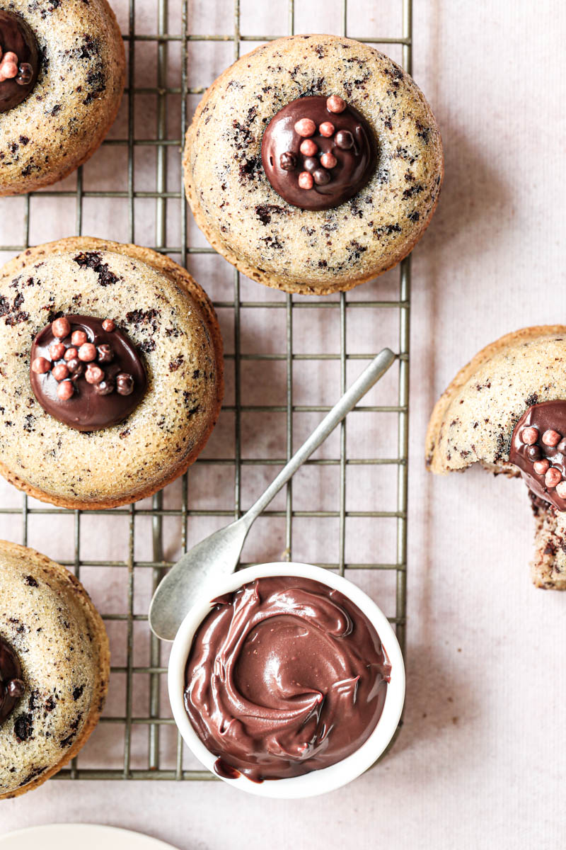 The mini chocolate chip financier almond cakes filled with chocolate ganache arranged on a wire rack with a small plate filled with the chocolate ganache on the right bottom corner.