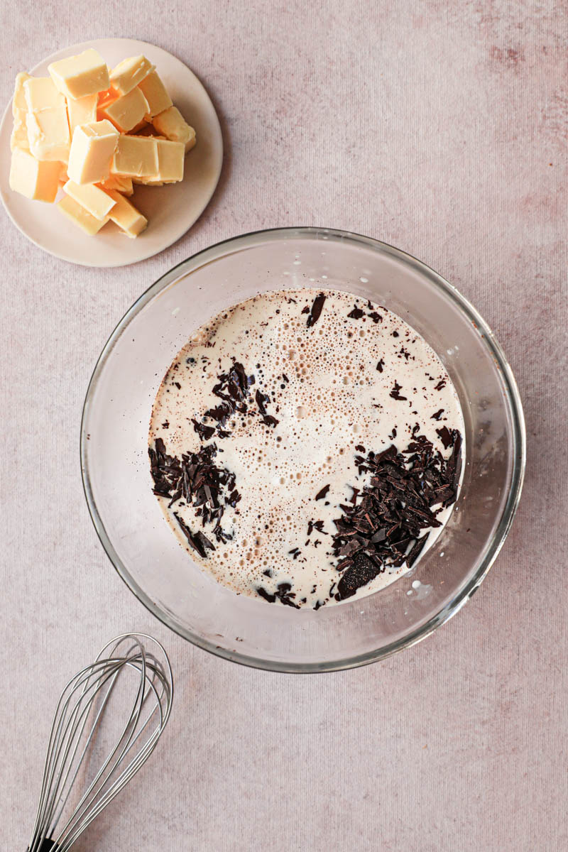 Chocolate ganache in the making: a glass bowl with the chocolate and the hot heavy cream with a small plate with butter on the side.