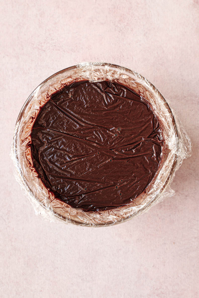 Chocolate ganache ready to set inside a glass bowl covered with plastic wrap.