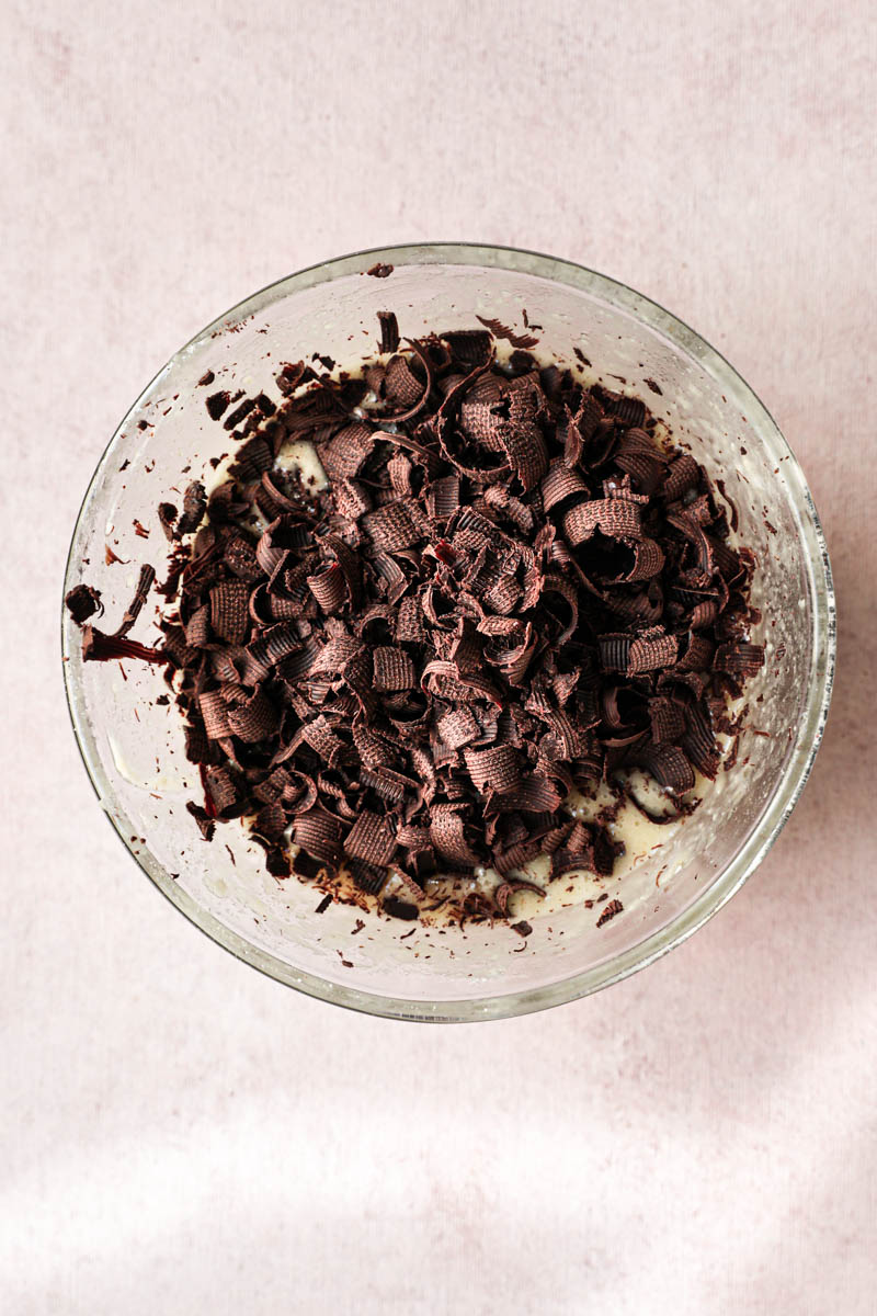 One glass bowl with the mini chocolate chip financier batter in the making: the mini almond financier cake batter with the chocolate shavings on top.