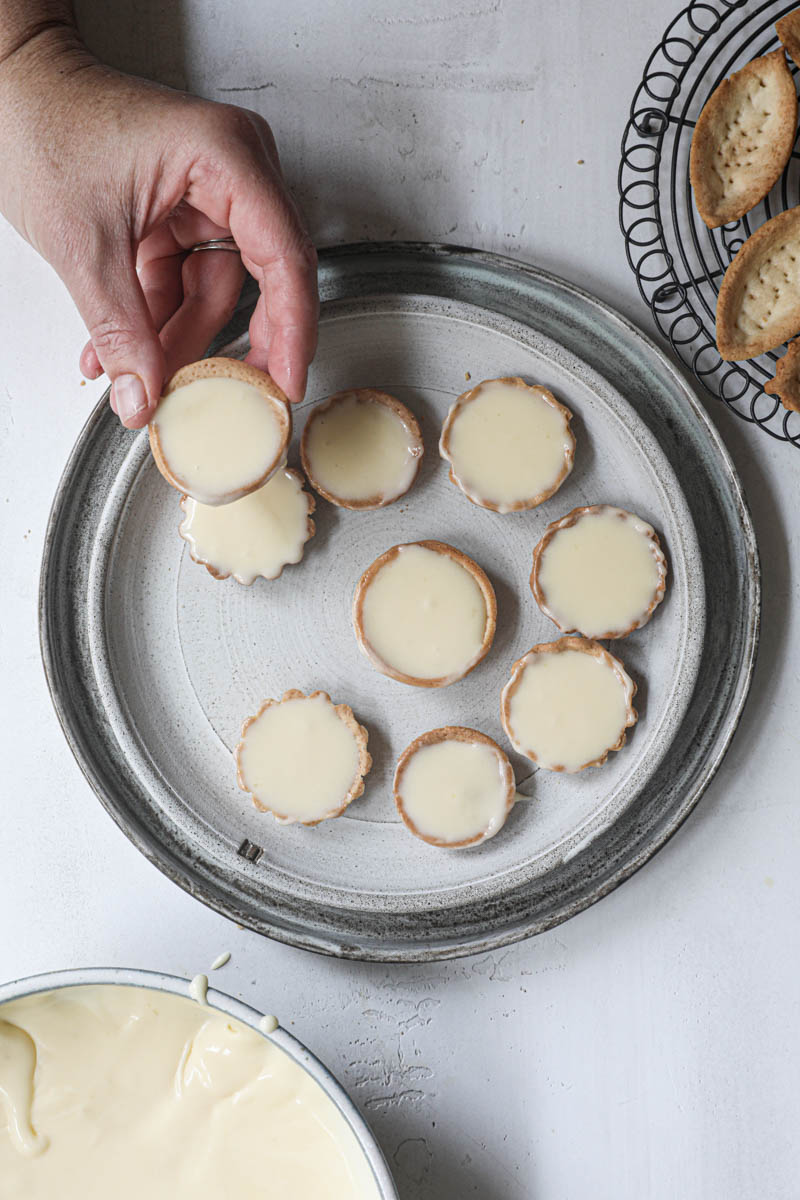One hand holding one mini lemon tartlet with others underneath it on a grey plate.