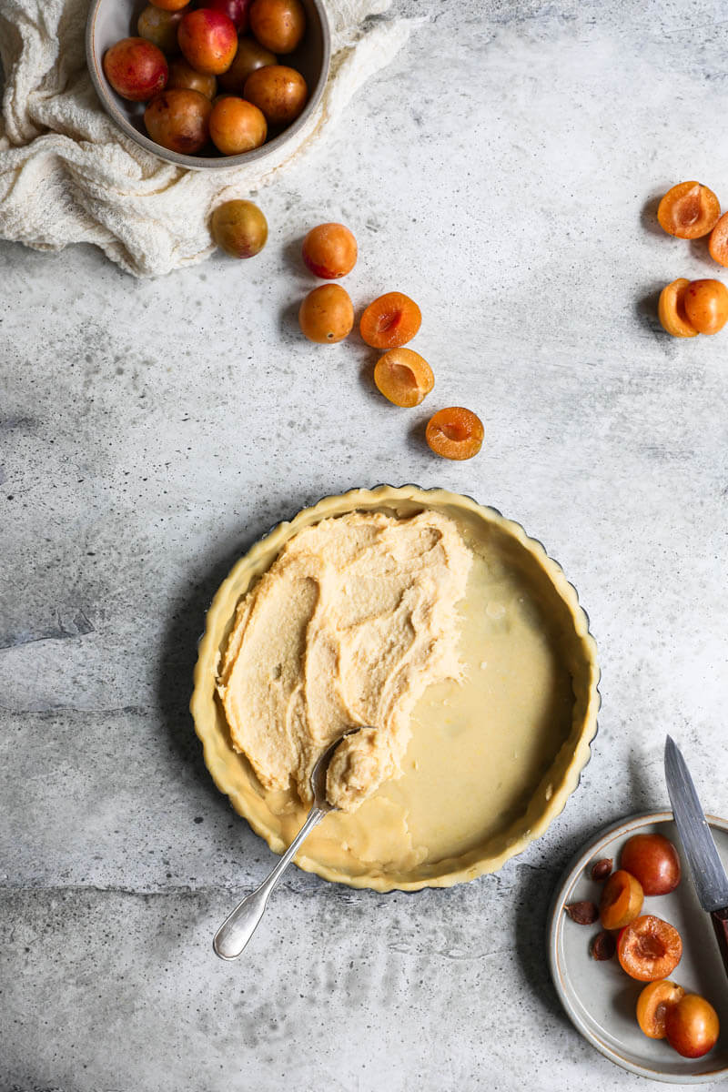 Overhead shot of the lined tart tin with the orange sable surrounded by sliced Mirabelle plums