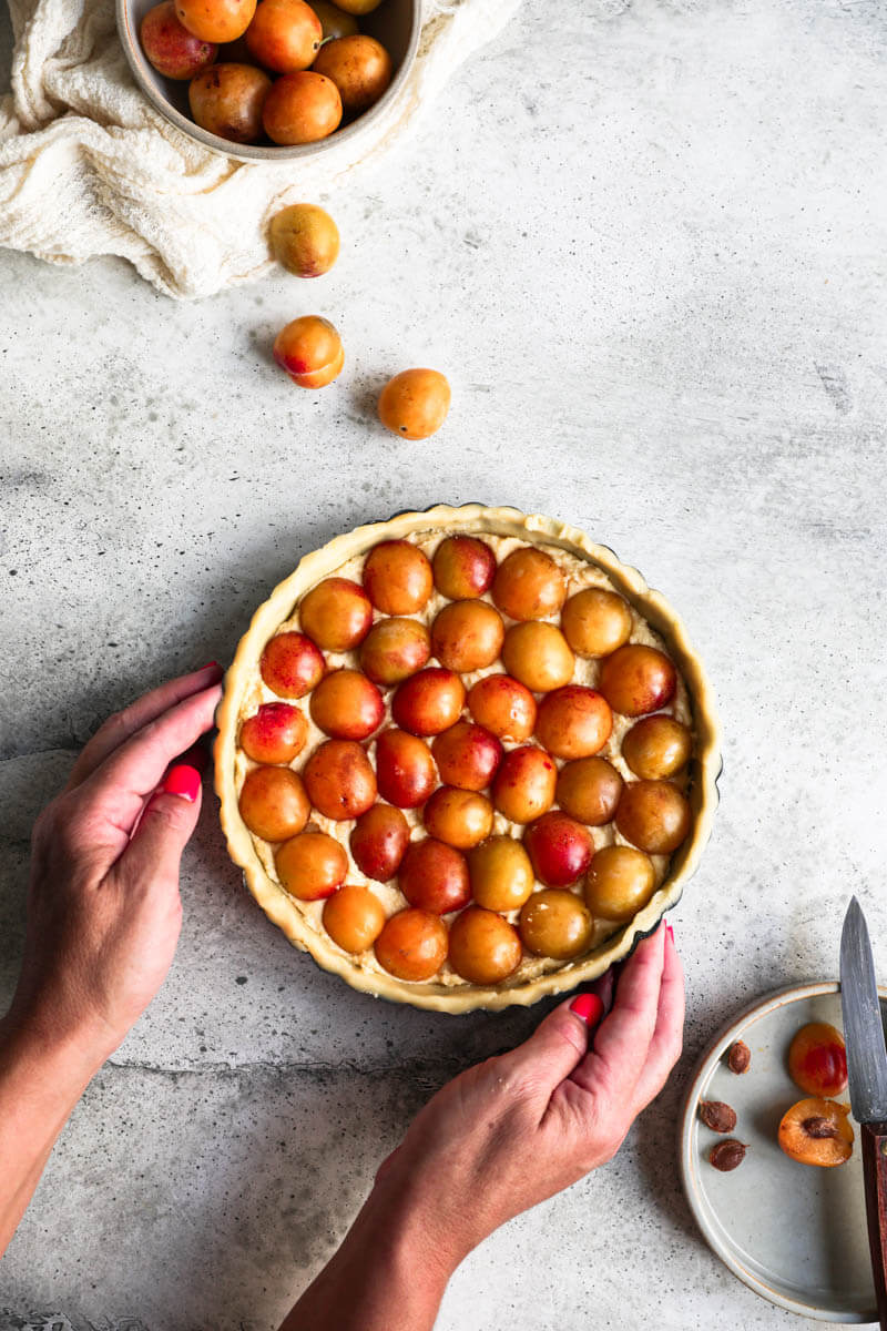 Overhead shot of two hands holding the Mirabelle plum tart ready for the oven