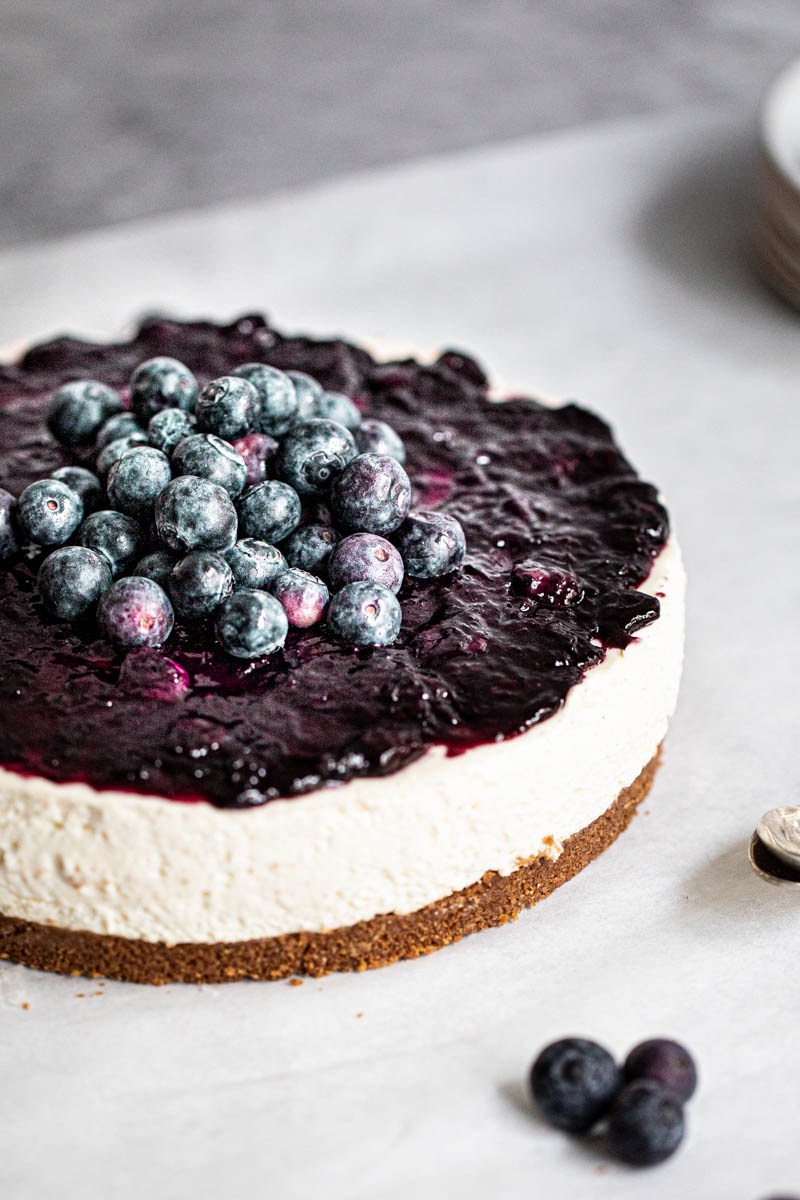 The whole fluffy no bake vanilla blueberry cheesecake with some blueberries on the front.