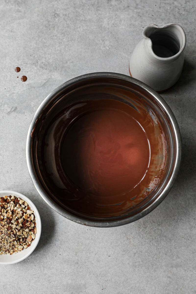 One bowl with melted chocolate and oil with a small bowl full of toasted chopped almonds and the side.