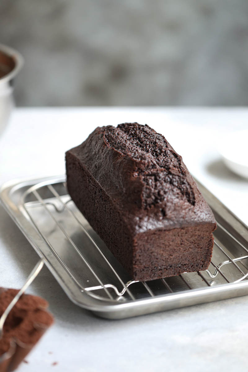 The baked one bowl chocolate cake cooling on a wire rack with a jar in the back.