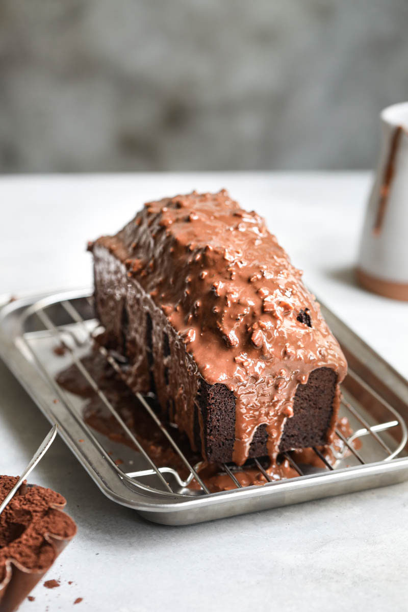 The glazed one chocolate bowl cake on a silver wire rack with a small jar in the back.