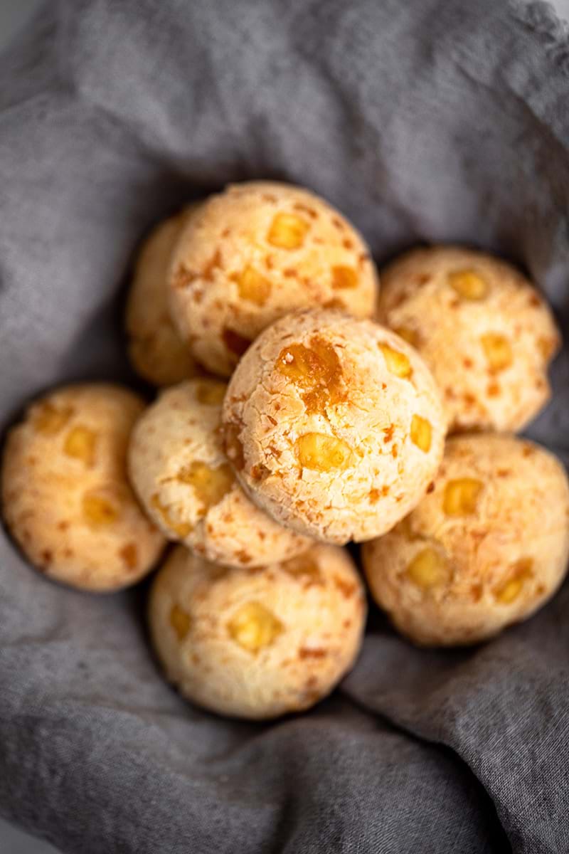Overhead shot of pao de queijo in a bowl covered with a linen