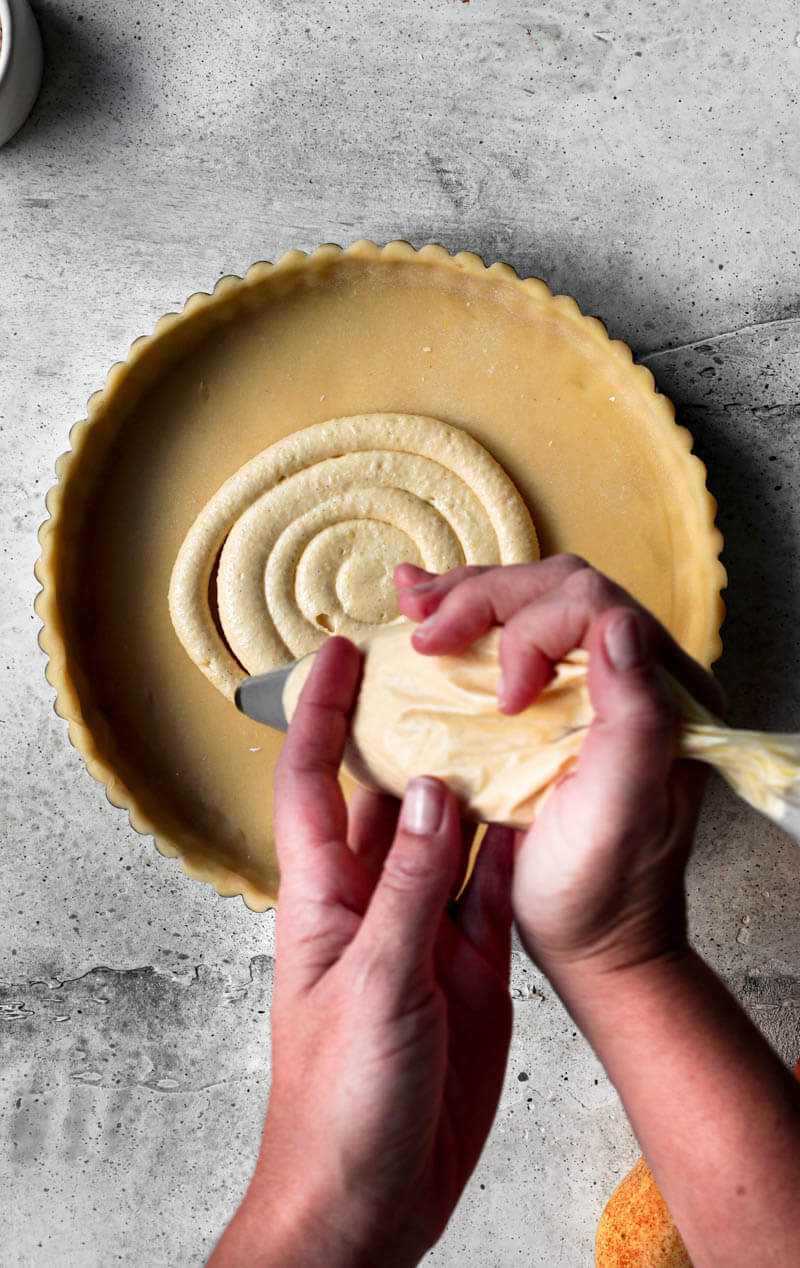 Overhead shot of 2 hands piping the frangipane inside the tart crust