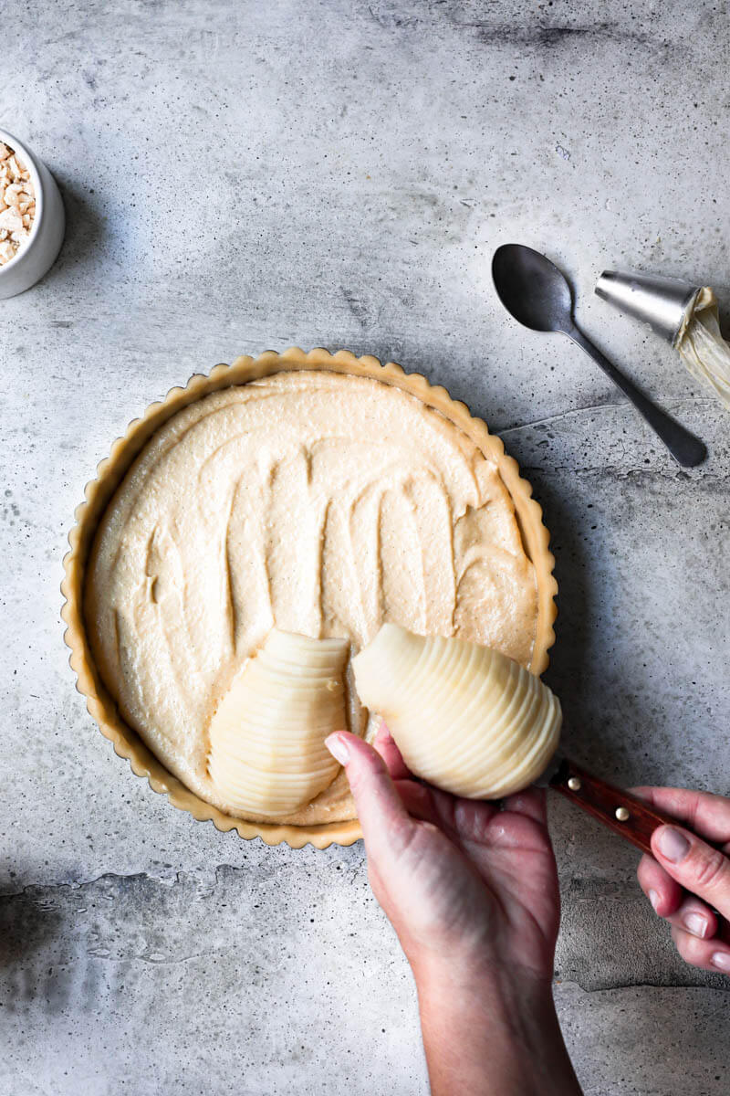 Overhead shot of 2 hands placing the sliced pear on top of the frangipane cream