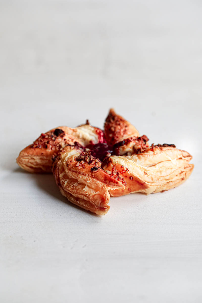 One raspberry pecan puff pastry pinwheel over white backdrop as seen from the side.