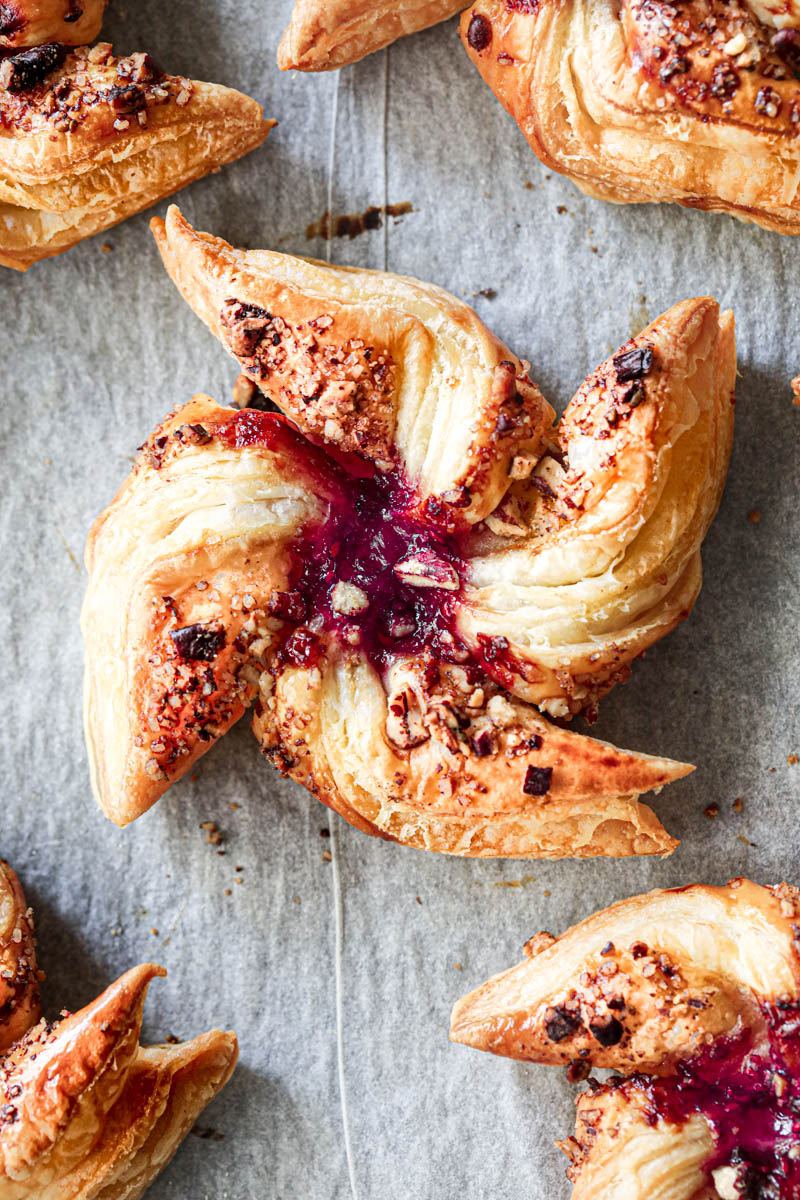 Closeup shot of one raspberry pecan puff pastry pinwheel with others on the side.
