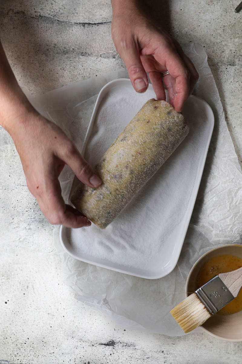 2 hands rolling the cookie dough log in sugar.