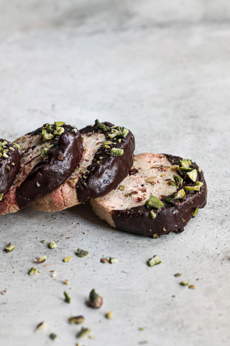 4 shortbread cookies dipped in chocolate drizzled with crushed pistachios placed in a domino effect manner seen from the side.