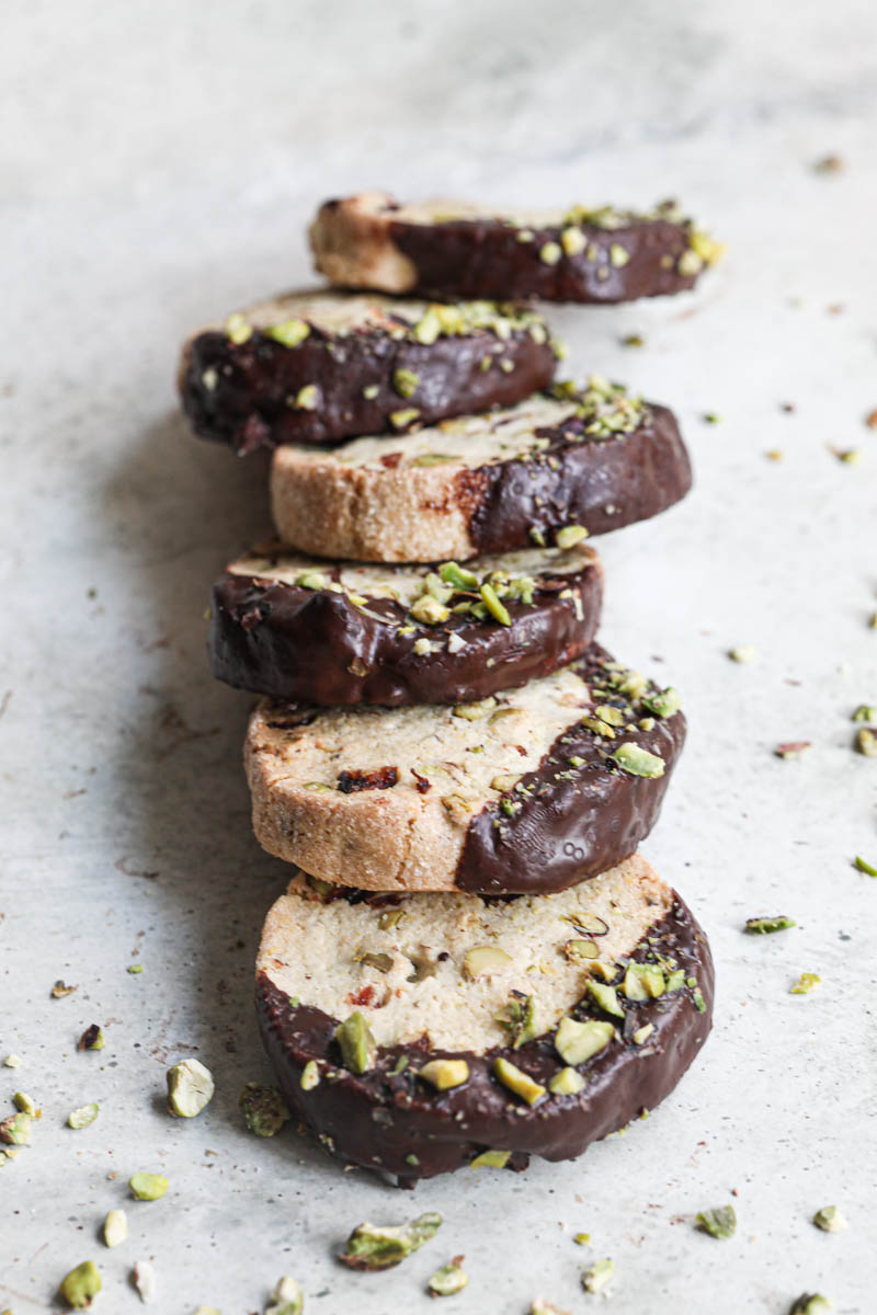 The shortbread cookies dipped in chocolate drizzled with crushed pistachios placed in a domino effect manner seen from the front.