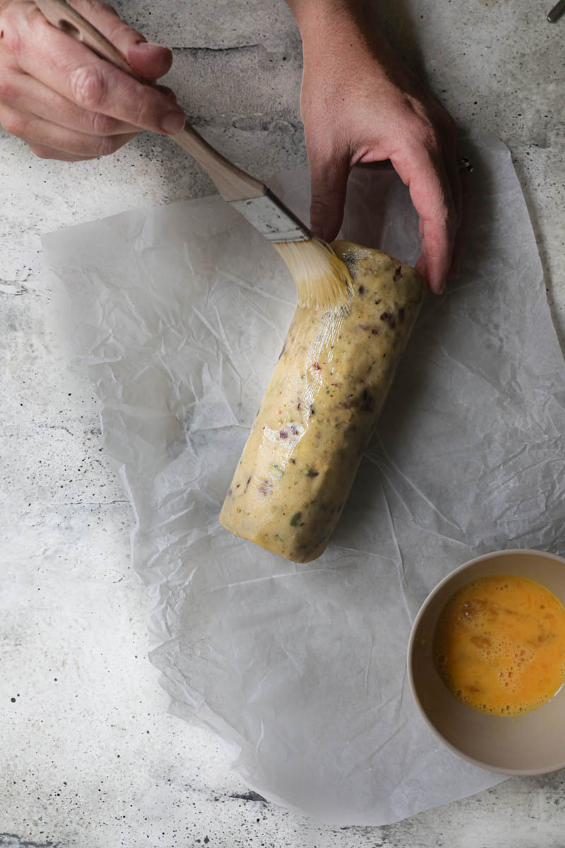 2 hands brushing the shortbread log with egg wash.