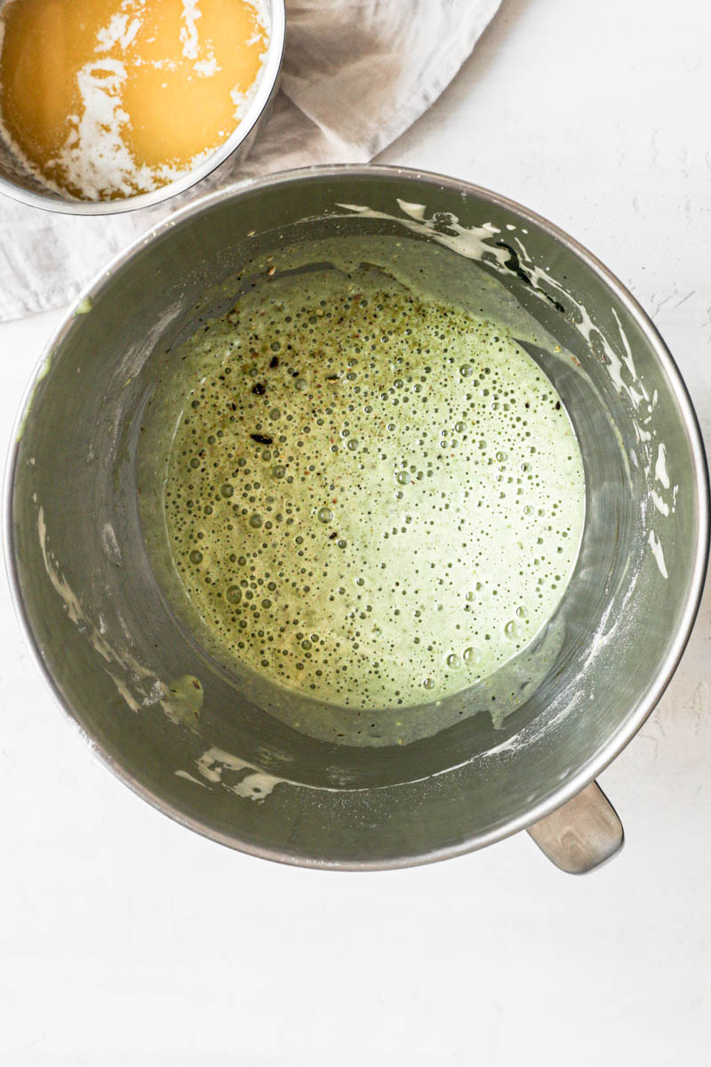 The pistachio madeleine batter inside a bowl with a small pan holding the melted butter.