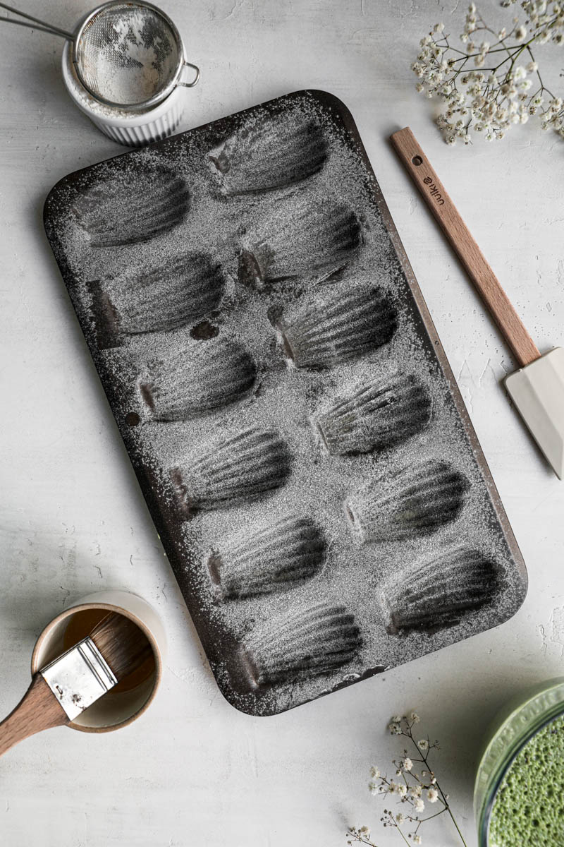 The madeleine pan buttered and floured with a brush, and small sift around it.