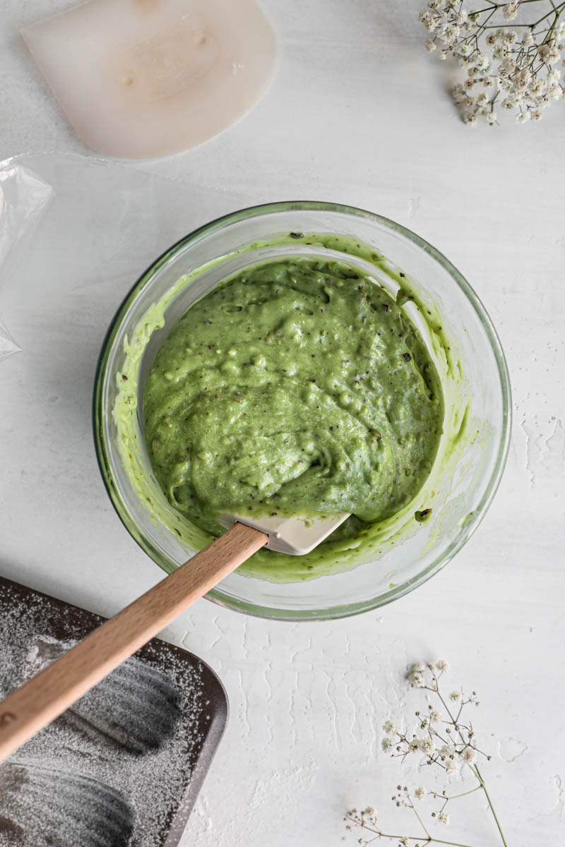 The chilled and smoothed out madeleine batter inside a glass bowl with a spatula in it.