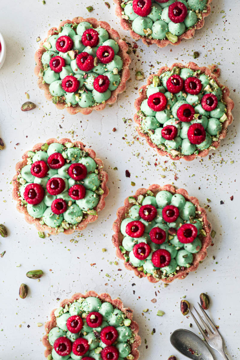 Pistachio raspberry white chocolate tartlets assembly: the tartlets topped with fresh raspberries filled with raspberry jam.