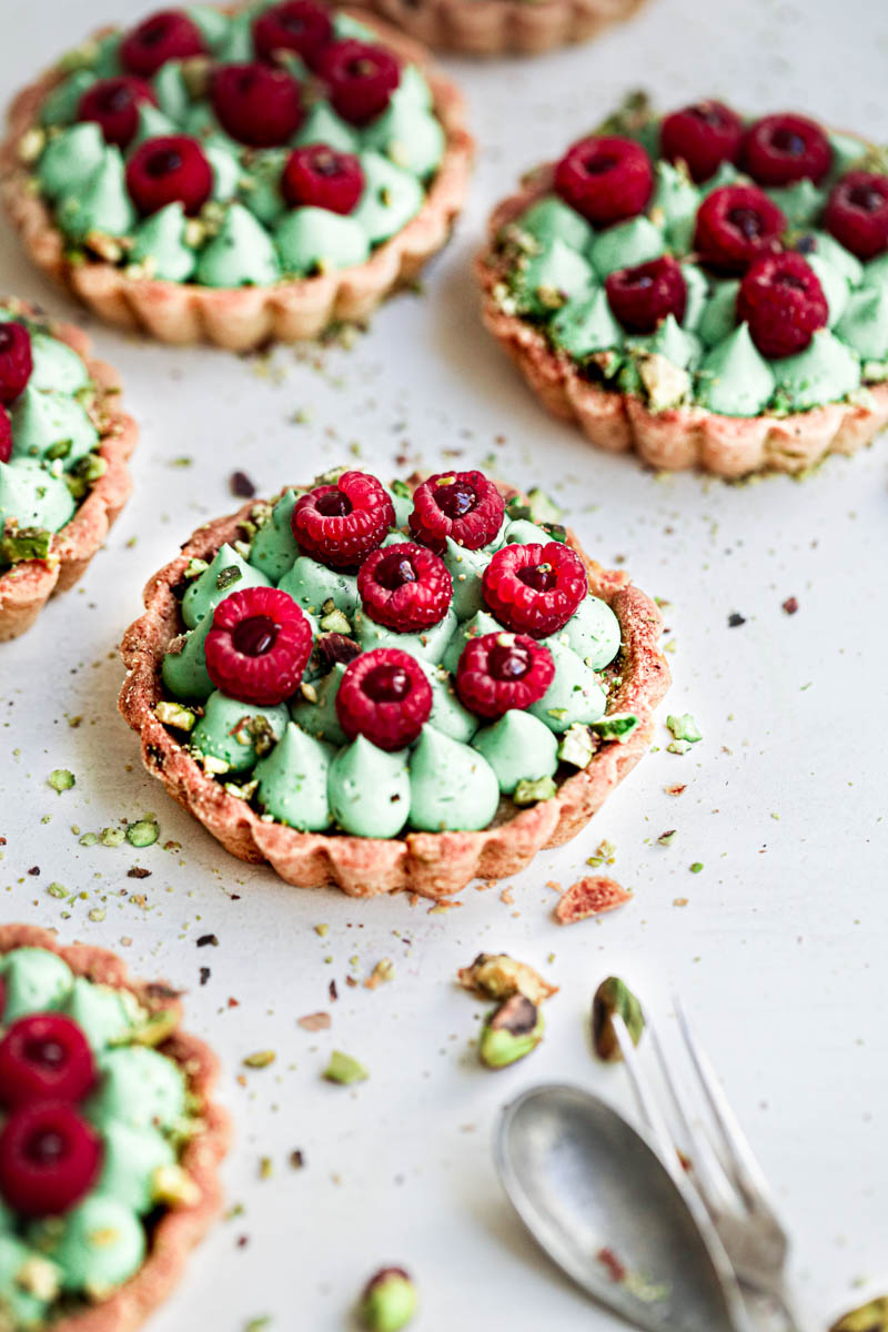 The pistachio raspberry white chocolate tartlets assembled topped with fresh raspberries seen from the side.