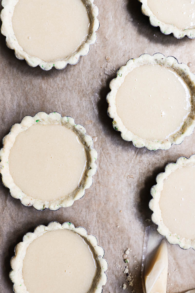 The tartlet tins lined with the pistachio shortbread crust filled with the financier batter.