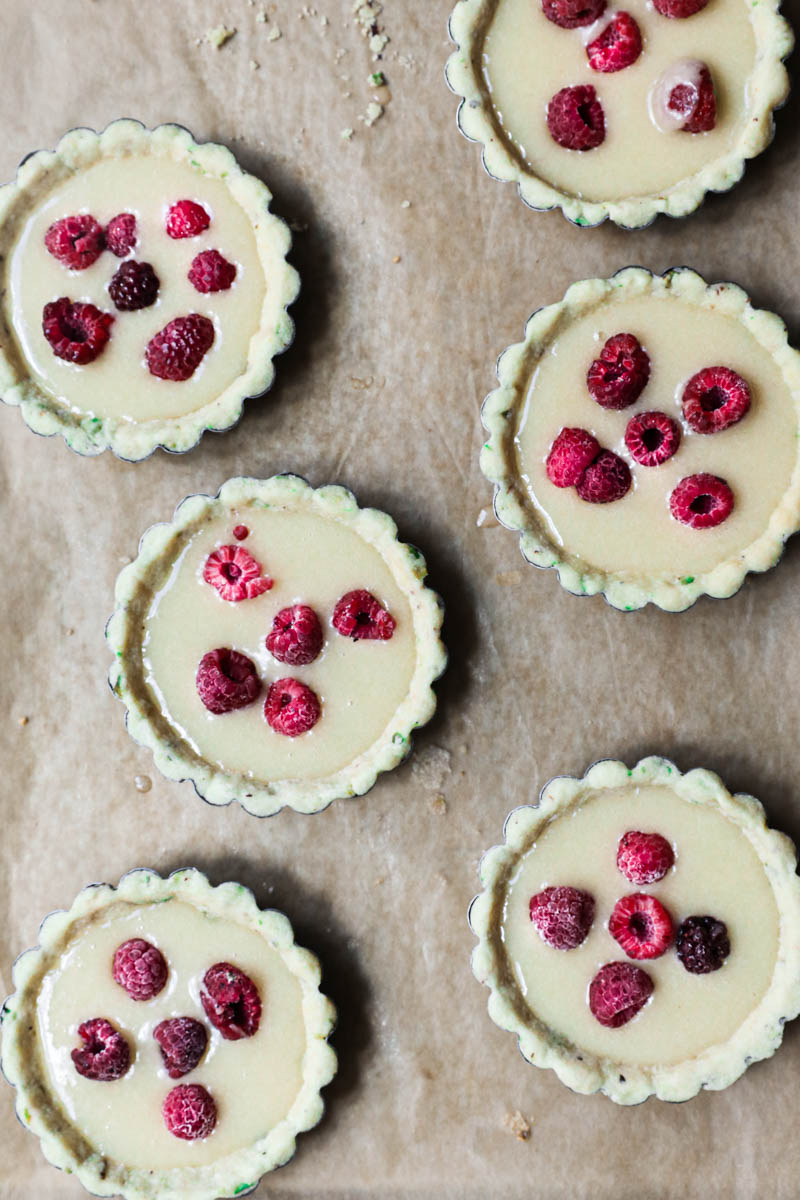 The tartlet tins lined with the pistachio shortbread crust filled with the financier topped with some raspberries.