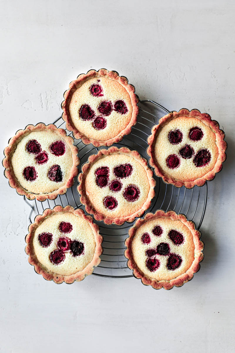 The baked pistachio raspberry tartlets on a round wire rack.