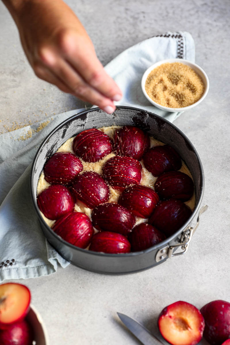 A hand sprinkling brown sugar over the plum cake